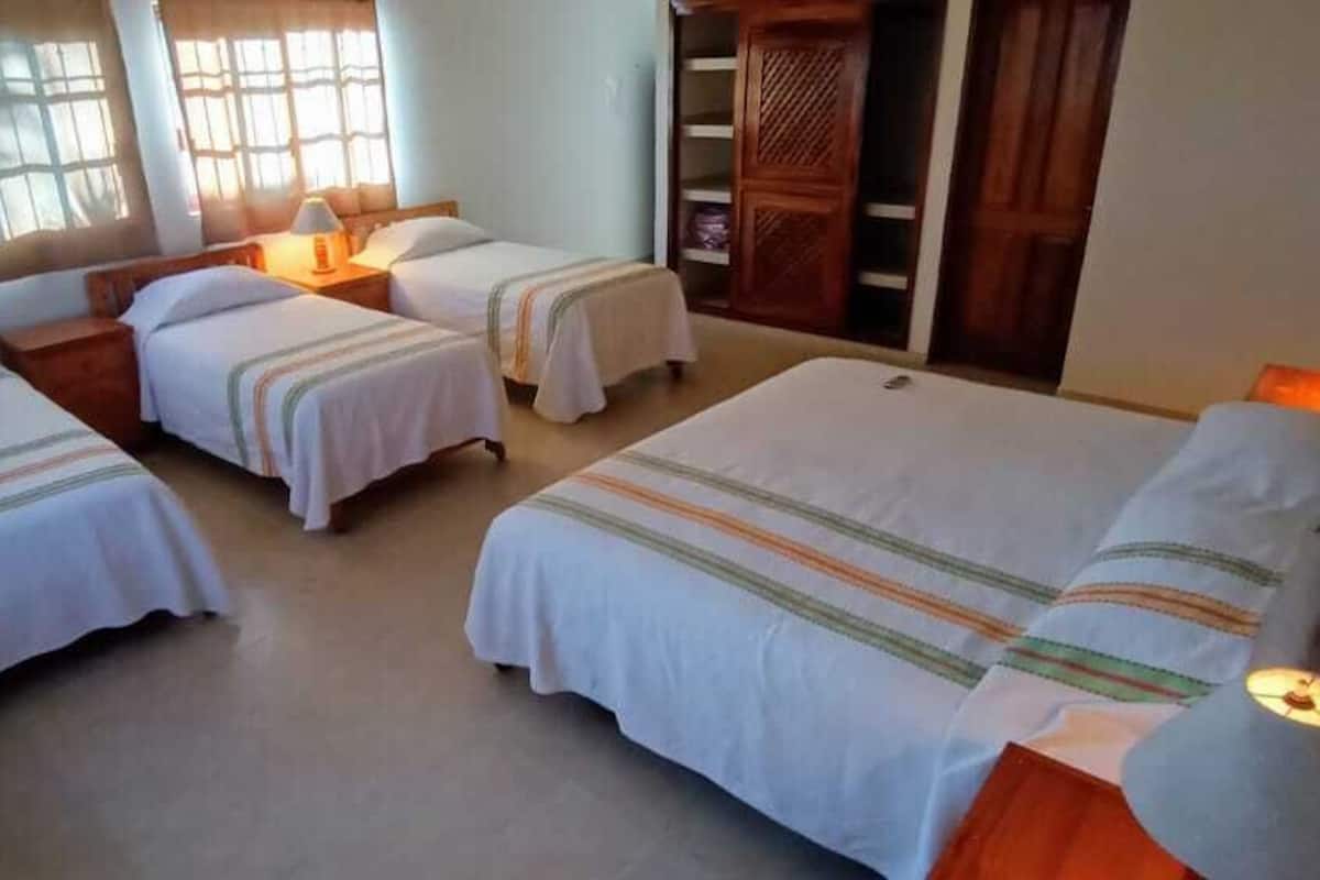 Une chambre d’hôtel avec quatre lits simples, une armoire en bois et une grande fenêtre avec des stores.