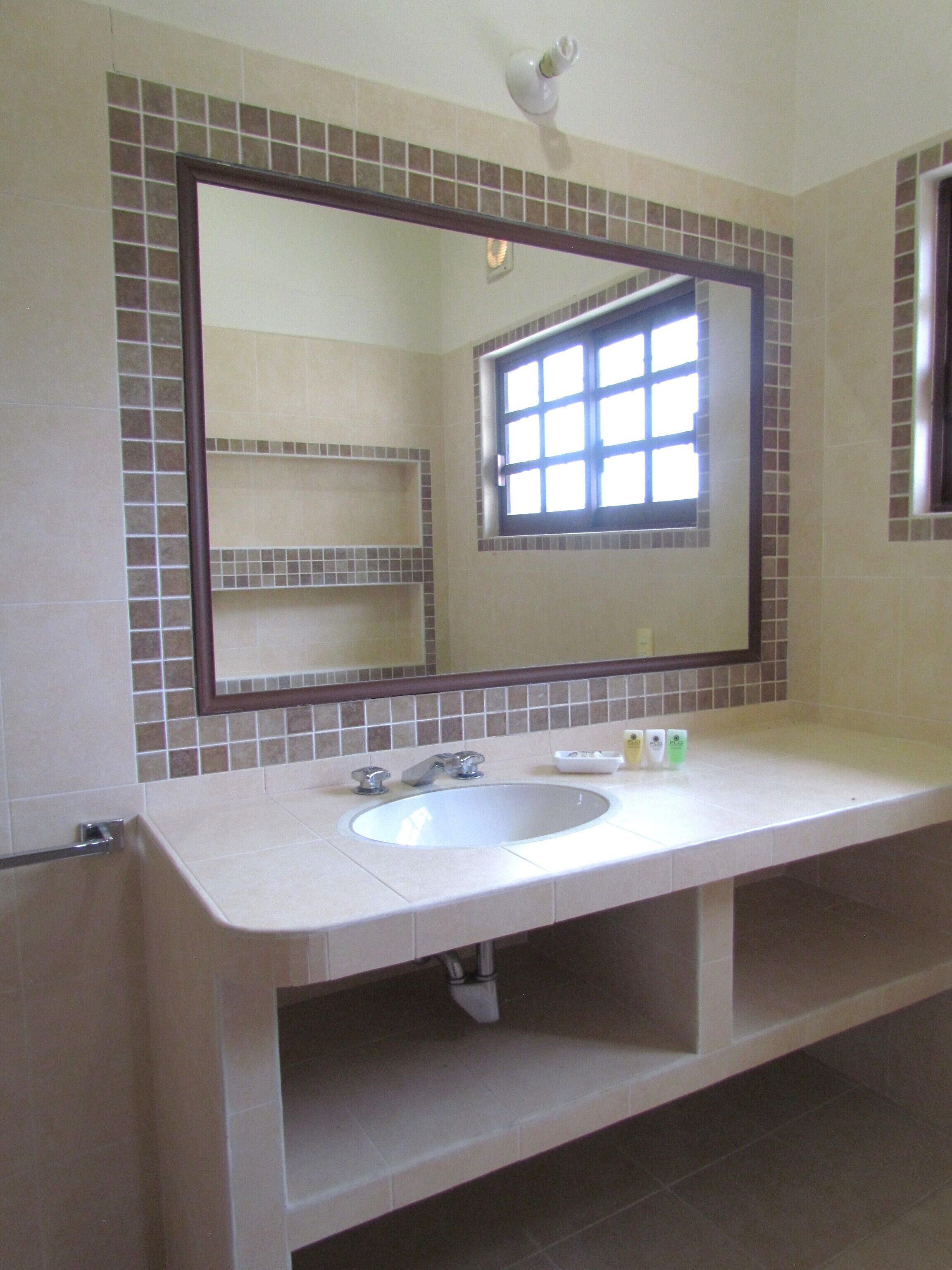 A bathroom with a large mirror, a sink, and a window.