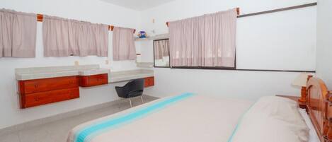 A bedroom with a bed, a desk, a chair, a vanity with a mirror, and a ceiling fan.