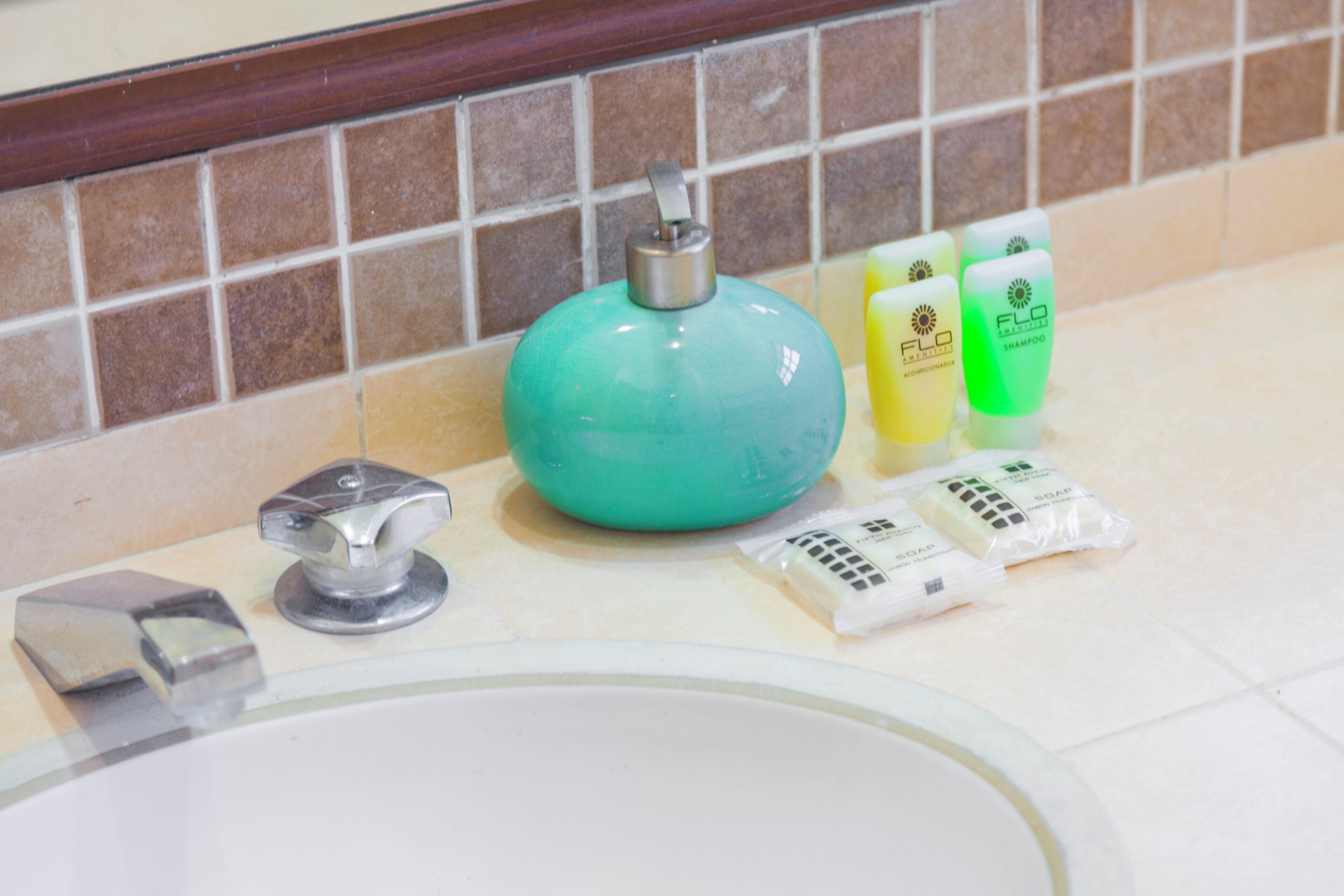 Uma pia de banheiro com artigos de higiene pessoal, incluindo um dosador de sabonete verde, garrafas de shampoo amarelas e verdes e um sabonete em barra.