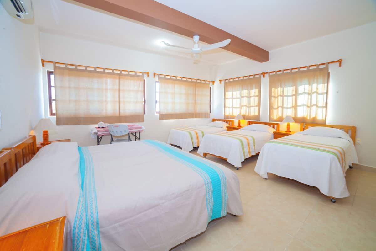 Une chambre d’hôtel avec trois lits simples, un ventilateur de plafond et une petite table avec des chaises.