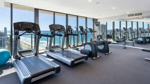Ein modernes Fitnessstudio mit mehreren Laufbändern und Trainingsgeräten, große Fenster mit Blick auf den Ozean.
