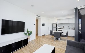 Un appartement moderne doté d’une télévision à écran plat, d’un coin repas, d’une cuisine et d’un salon avec un canapé.