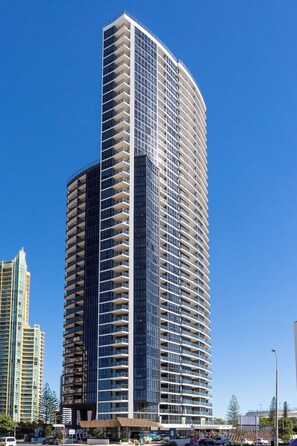 Um hotel moderno com vários varandas, design arquitetônico contemporâneo e um céu azul claro ao fundo.