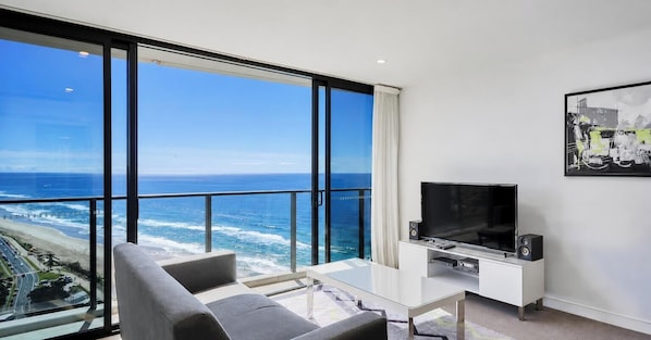 Una sala de estar moderna con un amplio ventanal con vistas al océano, un televisor de pantalla plana y un conjunto de mobiliario minimalista.