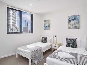 Une chambre d’hôtel moderne avec deux lits, une grande fenêtre donnant sur la ville et des œuvres d’art abstrait accrochées aux murs.