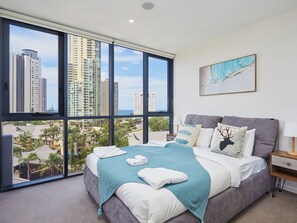 A bedroom with a large window, a bed with a teal blanket, and a city view.