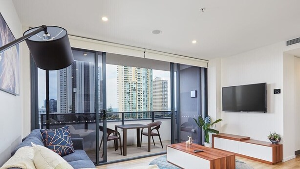 Een moderne woonkamer met een bank, salontafel, televisie en een balkon met uitzicht op de stad.