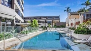 A swimming pool with clear blue water, surrounded by a glass railing and white lounge chairs. - Bright Open view 2 bedroom Apartment in Gold Coast (Surfers Paradise)