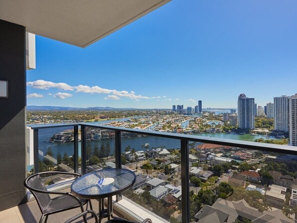 A balcony with a glass railing overlooking a cityscape, a table, and chairs.