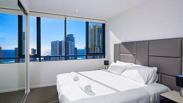 A modern hotel room with a large bed, a nightstand, and a view of tall buildings through large windows.