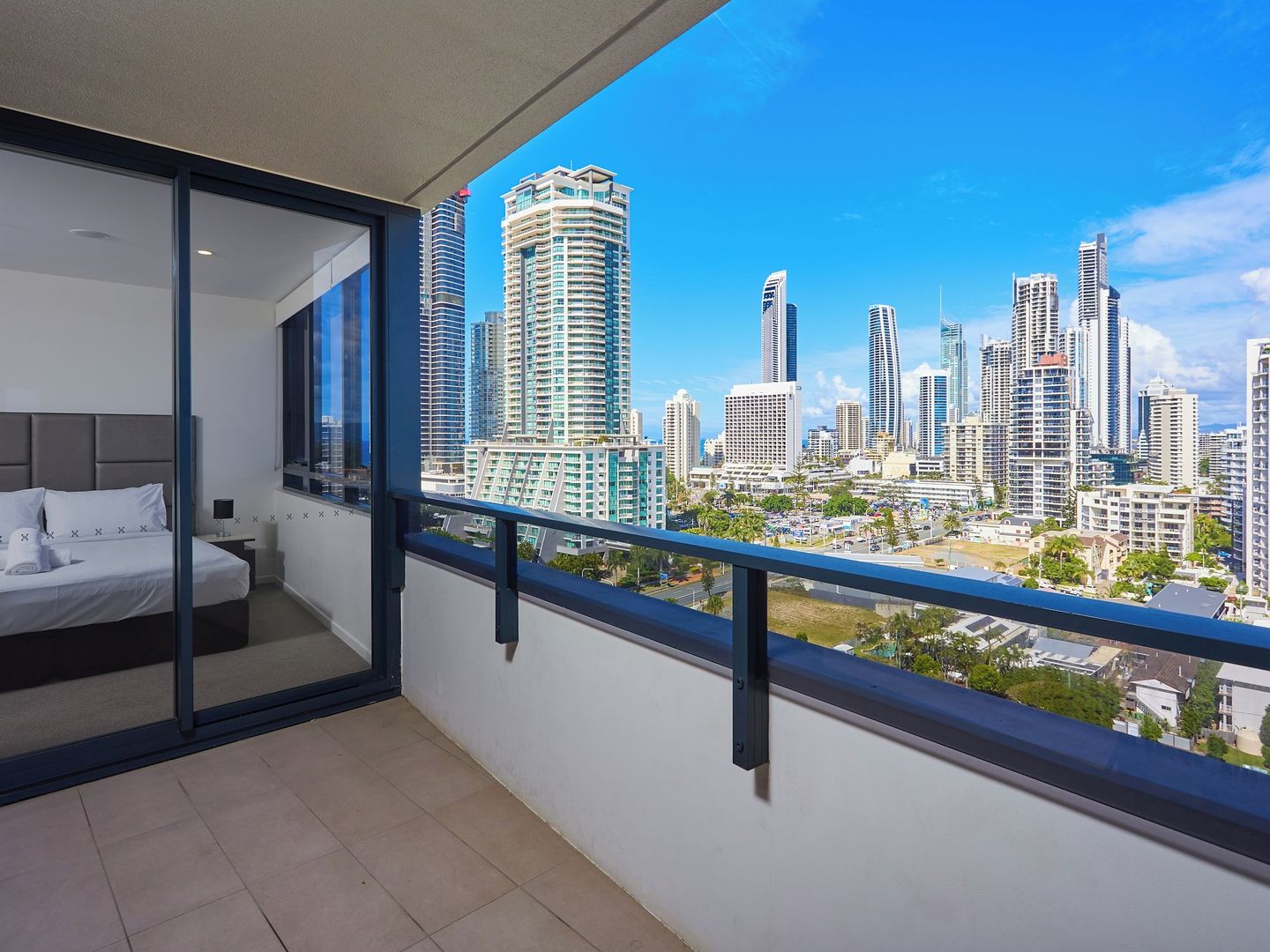 A bedroom with a city view, a bed, a nightstand, and a window with a balcony.