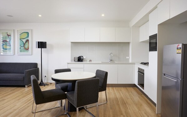 A modern kitchen with white cabinets, a stainless steel refrigerator, a round dining table with four chairs, and a black floor lamp.