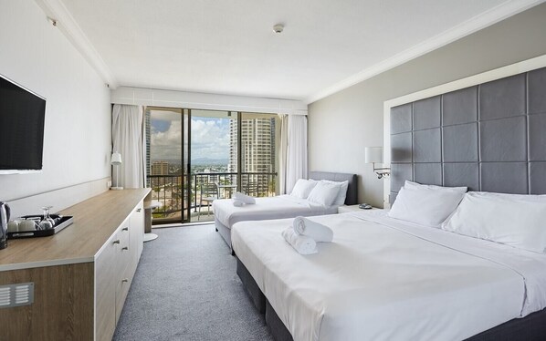 Een hotelkamer met twee bedden, een bureau, een televisie en een balkon met uitzicht op de stad.