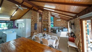 A rustic kitchen with a brick wall, wooden ceiling beams, and a dining area with a wooden table and chairs.