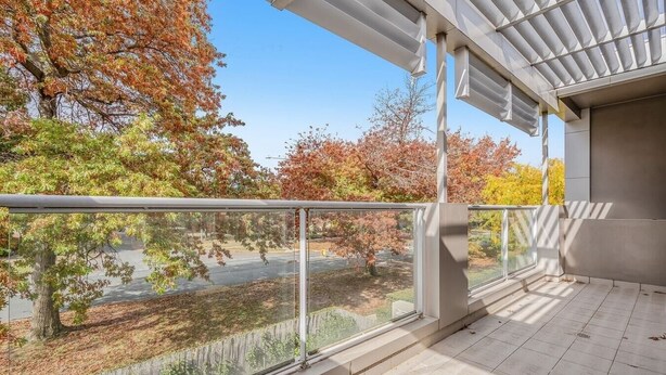 Ein Balkon mit Glasgeländer mit Blick auf einen Park mit Herbstbäumen.