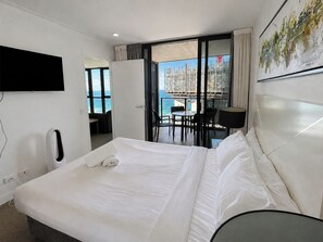 Habitación de hotel con cama, televisión, escritorio y balcón con vista al mar y una obra en construcción.