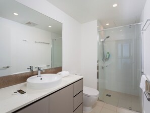 Un baño moderno con un espejo grande, un lavabo, un inodoro y una ducha con mampara de vidrio.