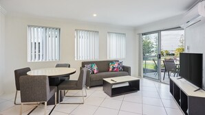 A modern living room with a round dining table, grey sofa, and a TV on a stand.