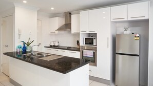 A modern kitchen with white cabinets, a black countertop, stainless steel appliances, and a built-in oven.