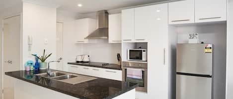 A modern kitchen with white cabinets, a black countertop, stainless steel appliances, and a built-in oven.