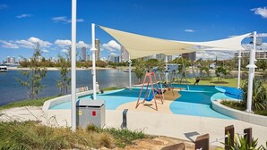 A waterfront park with a swimming pool, swings, and a large canopy.