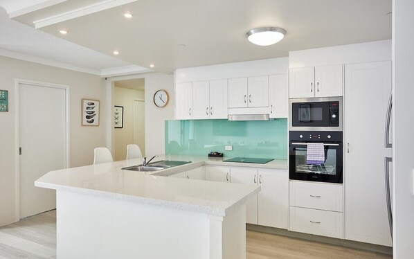 Una cocina moderna con armarios blancos, una isla central, un microondas, un horno y un reloj en la pared.