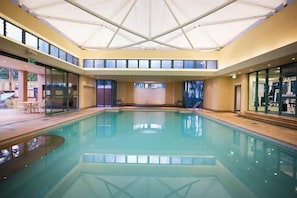 A large indoor swimming pool with a glass ceiling and a view of the outside.
