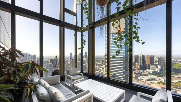 A high-rise interior with large windows, a white sofa, a small table, and hanging plants.