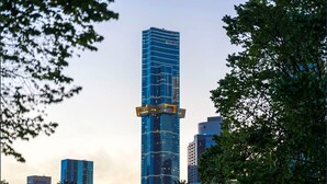A tall, modern skyscraper with a glass facade, surrounded by trees and other buildings.