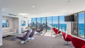 Ein modernes Hotelzimmer mit großen Fenstern, das Blick auf Stadt und Meer bietet, inklusive Flachbildfernseher und zeitgemäßem Sitzmöbel.