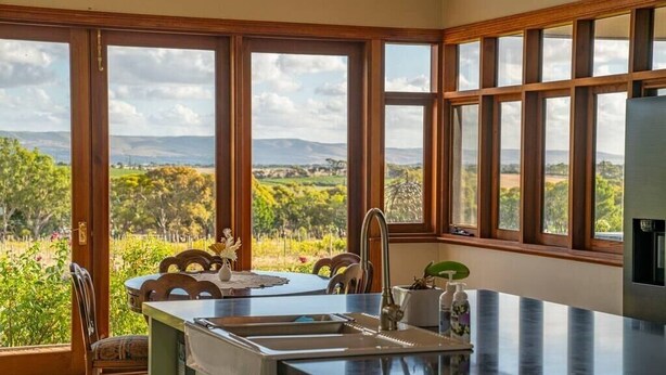 A kitchen with large windows, a sink, and a dining area with chairs. - Condor Estate Spacious with Vineyard and Fireplace (Maslin Beach)