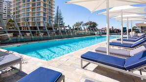 A swimming pool with lounge chairs and umbrellas, surrounded by a high-rise building.