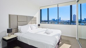 Une chambre d’hôtel moderne avec un grand lit, une table de chevet, une lampe et une vue sur la ville grâce à de grandes fenêtres.
