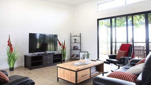 A modern living room with a flat-screen TV, a wooden coffee table, black leather sofas, and a large window offering a view of greenery. - The Red Door @ Barossa Valley ★Vineyard View★ (Nuriootpa)