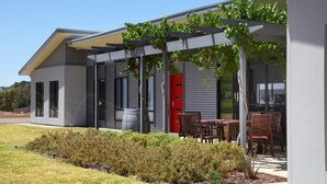 A modern building with a covered patio area, outdoor seating, and a well-maintained garden. - The Red Door @ Barossa Valley ★Vineyard View★ (Nuriootpa)
