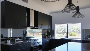A modern kitchen with dark cabinetry, a large island, and a view of the outdoors. - The Red Door @ Barossa Valley ★Vineyard View★ (Nuriootpa)