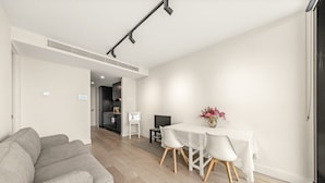 Ein modernes Wohnzimmer mit einem grauen Sofa, einem Esstisch mit weißen Stühlen und einer Küche im Hintergrund.