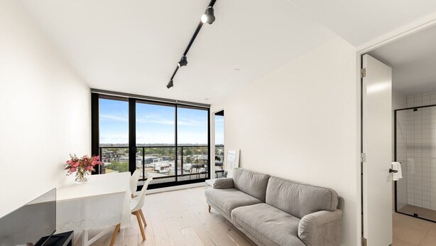 Ein modernes Wohnzimmer mit großem Fenster, einem grauen Sofa, einem weißen Tisch und einem Fernseher.