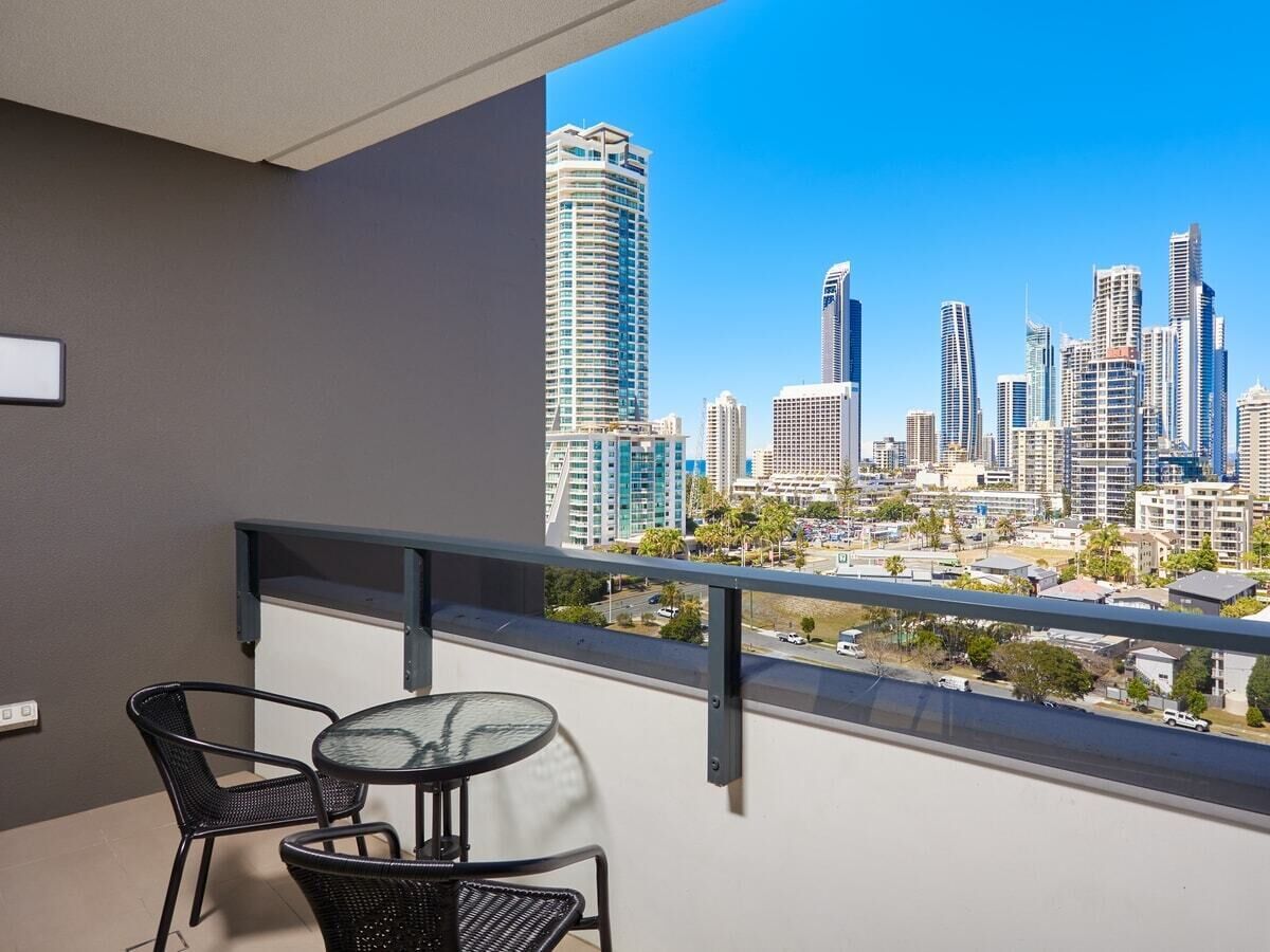 A balcony with a view of a city skyline, a round table, and two chairs.