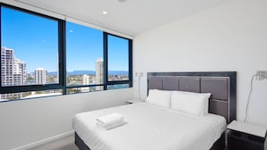 A modern hotel room with a large bed, a nightstand, and a view of the city skyline through large windows.