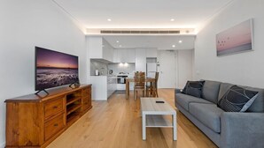 Un salon moderne doté d’un téléviseur à écran plat, d’un meuble de rangement en bois, d’un canapé gris et d’un coin repas avec une table et des chaises.