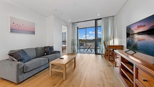 Un salon moderne avec un canapé gris, une table basse en bois et un téléviseur posé sur un meuble en bois.