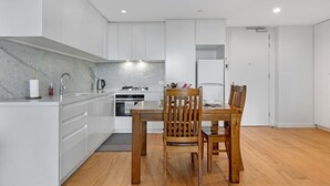 Une cuisine moderne avec des meubles blancs, une table à manger entourée de chaises en bois et un four encastré.
