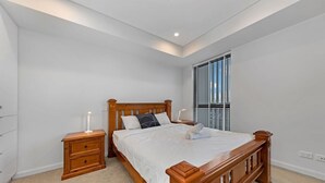 Une chambre à coucher avec un lit en bois, deux tables de chevet, une commode, une fenêtre avec des stores et un luminaire au plafond.