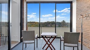 Un balcon avec une table et deux chaises, de grandes portes vitrées et une vue sur le ciel et le paysage lointain.