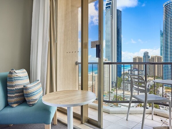 A balcony with a sofa and chairs, overlooking a cityscape with tall buildings and a view of the ocean.
