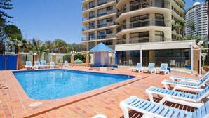 A hotel pool area with lounge chairs and a building with multiple balconies.