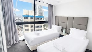 A hotel room with two beds, a grey headboard, and a view of the cityscape.