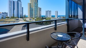 Un balcon avec une table et des chaises, donnant sur un paysage urbain avec de hauts immeubles et une plage.